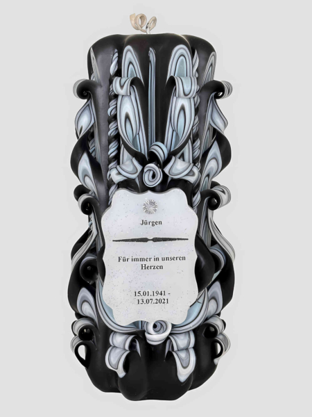 handgeschnitzte schwarze Kerze mit kunstvollem Schnitzdesign. Innenschichten sind in hellblau-grau gestaltet. Unten mittig ist ein personalisiertes Schild sichtbar