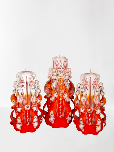 Drei handgeschnitzte Devela Kerzen im 3er-Set, sechseckig und kegelförmig, in warmen Orange- und Rottönen mit filigranen Ornamenten. Eine Kerze ist 21 cm hoch, zwei sind 18 cm hoch – ideal als Herbst-Deko oder luxuriöses Geschenk