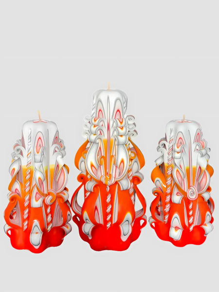 Handgefertigte, kunstvoll geschnitzte Kerzen in Orange, Weiß und Gelb auf weißem Hintergrund.