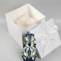 Dunkelblaue handgeschnitzte Kerze neben Weißem Geschenkbox mit Deckel, Box ist quadratisch.