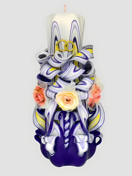 Handgeschnitzte Hochzeitskerze in Violett-Weiß mit goldenen Eheringen und zarten Rosa-Blumen vor hellem Hintergrund. Bild von Vorne
