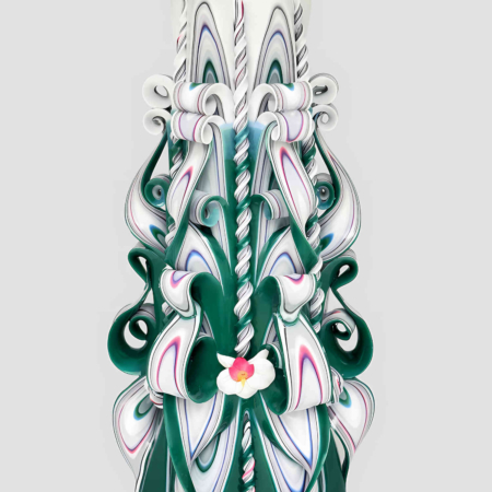 Handgeschnitzte grüne Kerze mit weißen und blauen Wellenmustern, spiralförmigen Verzierungen und zentraler rosa Blume vor hellem Hintergrund
