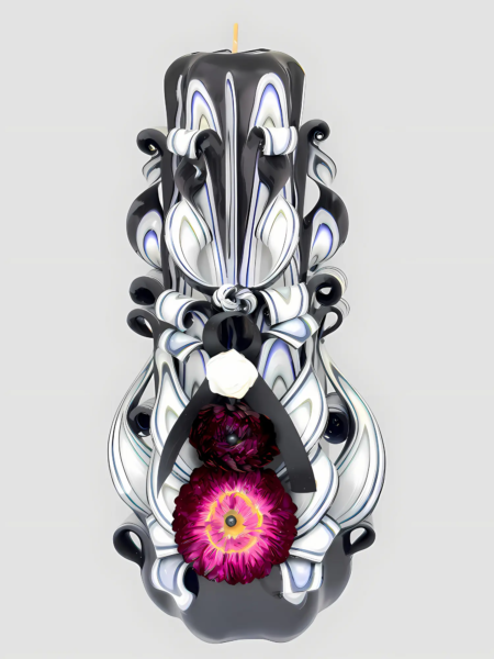 Handgeschnitzte schwarze Trauerkerze mit weißen und blauen Wellenmustern sowie zentraler pinkfarbener Blume vor hellem Hintergrund.