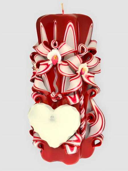 Handgeschnitzte rote Love-Kerze mit weißen Bändern aus Paraffin, Orchideen, einem leeren weißen Herzen und spiralförmigen Verzierungen vor hellem Hintergrund.