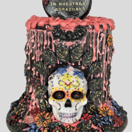 Handmodellierte und handbemalte Halloween-Kunstkerze von Devela Kerzenmanufaktur mit mexikanisch inspiriertem Totenkopf, bunten Blumen, schwarzen Ornamenten und rosa Wachselementen. Auf dem Herz steht: "Siempre en nuestros corazones"