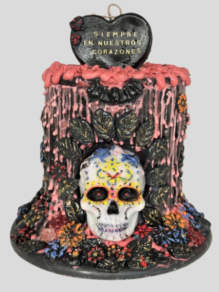 Handmodellierte und handbemalte Halloween-Kunstkerze von Devela Kerzenmanufaktur mit mexikanisch inspiriertem Totenkopf, bunten Blumen, schwarzen Ornamenten und rosa Wachselementen. Auf dem Herz steht: "Siempre en nuestros corazones"